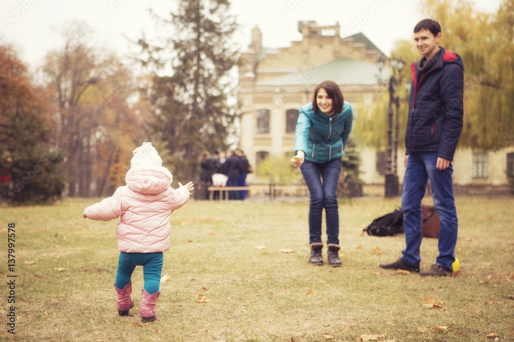 Happy loving family(mother, father and little daughter kid) outdoors walking having fun on a park in autumn season. Fallen yellow leaves on a background. Cold weather