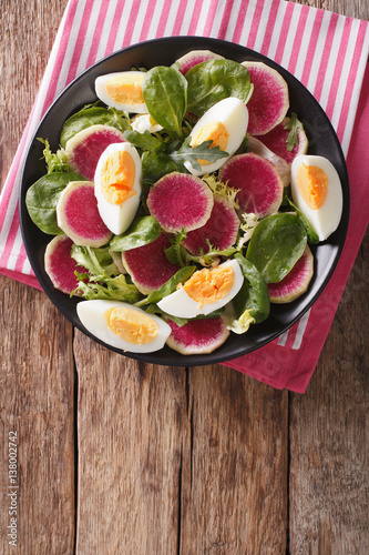 Tasty salad of watermelon radishes, eggs, spinach and herbs closeup. vertical top view