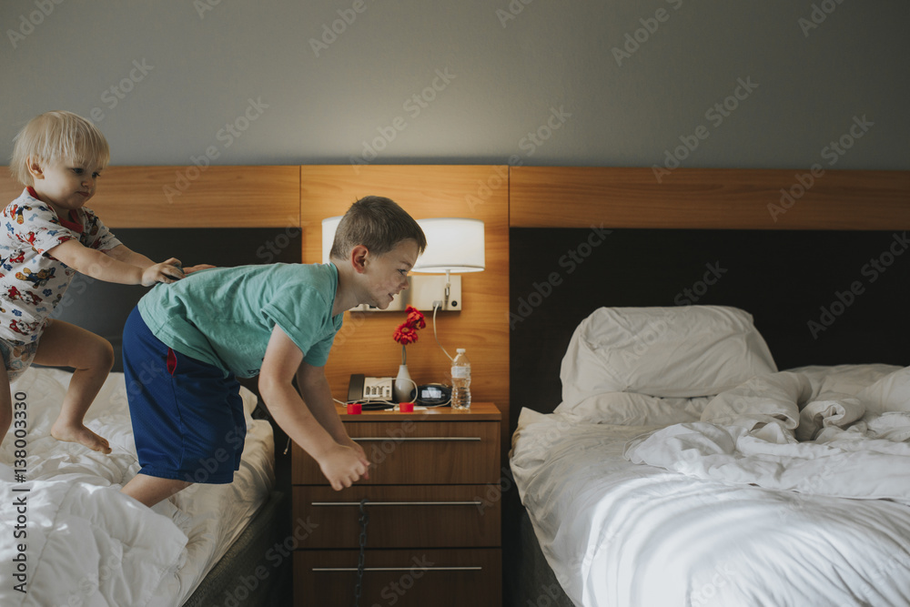 Boy pushing brother jumping from bed at home Boy pushing brother jumping from bed at home