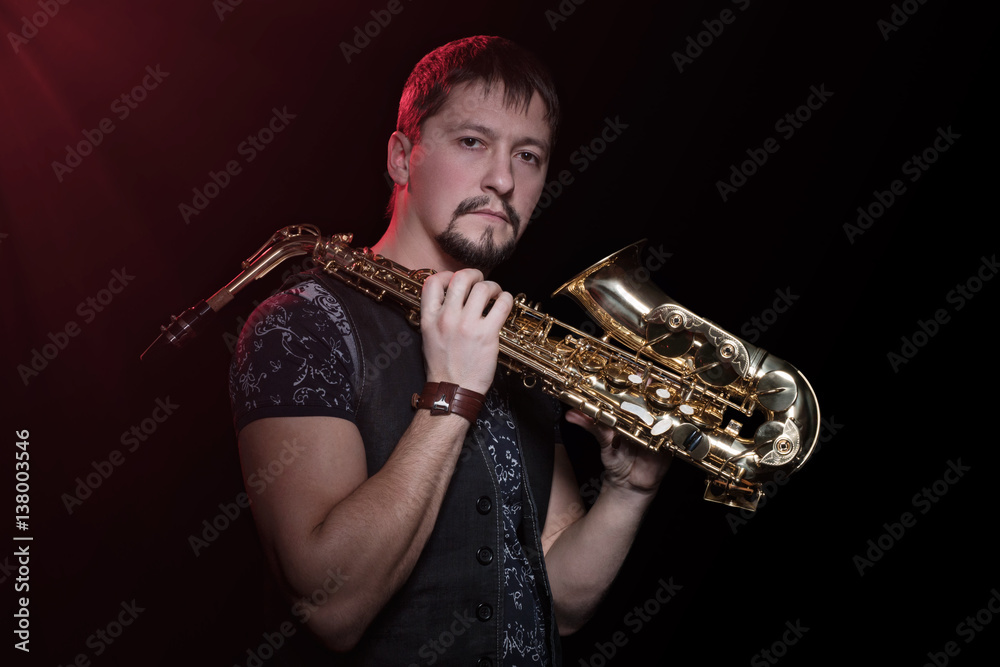 Naklejka premium Serious bearded saxophonist with sax on the shoulder isolated against a black background