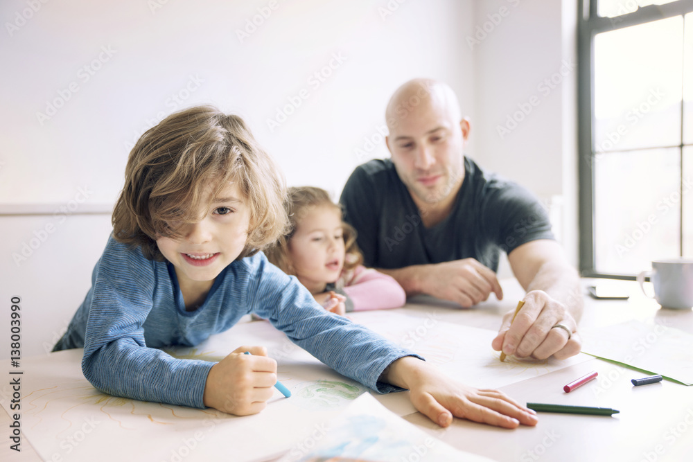Portrait of boy drawing while father assisting daughter at table in home Portrait of boy drawing while father assisting daughter at table in home