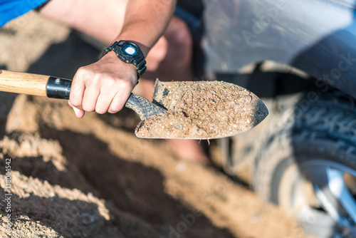 a man digs a car stuck in the sand, throwing sand shovel out from under the car