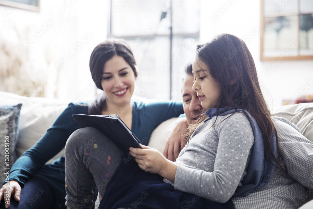 Father and mother looking at daughter using tablet computer while sitting on sofa at home Father and mother looking at daughter using tablet computer while sitting on sofa at home