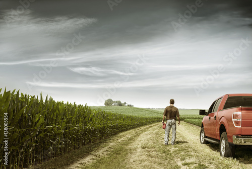 Rear view of farmer standing by car on field against cloudy sky