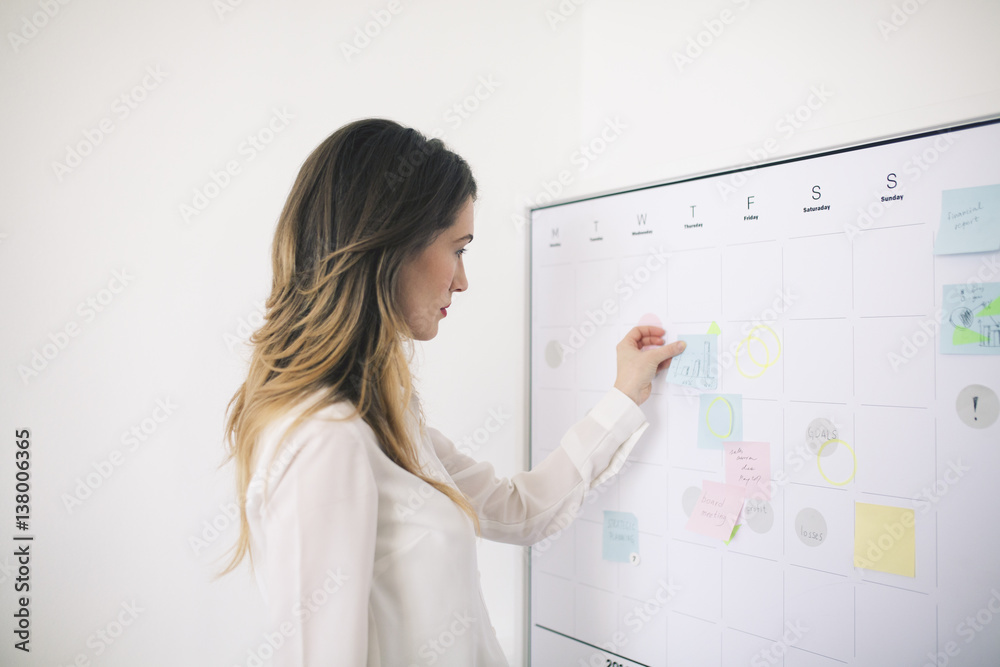 Side view of businesswoman sticking adhesive notes on whiteboard in office Side view of businesswoman sticking adhesive notes on whiteboard in office