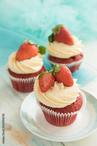 Three pink white cupcakes with strawberries on a blue wooden table. Selective focus