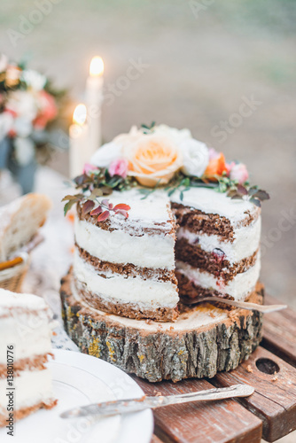 Beautiful sliced wedding cake decorated with flowers on wooden circle outdoor
