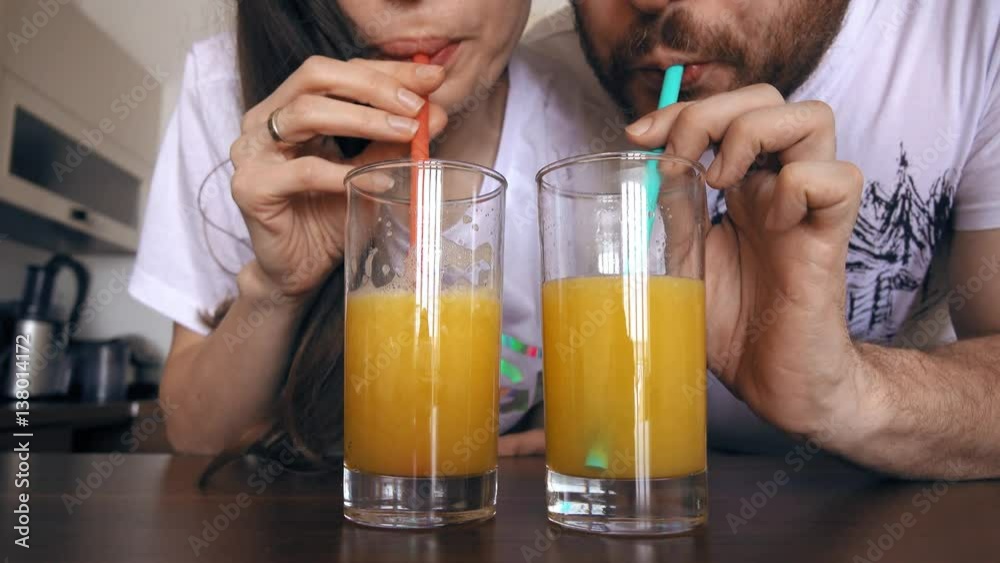 Young woman and man drinking orange juice with straws. Healthy lifestyle or funny competition concepts. 4K clip