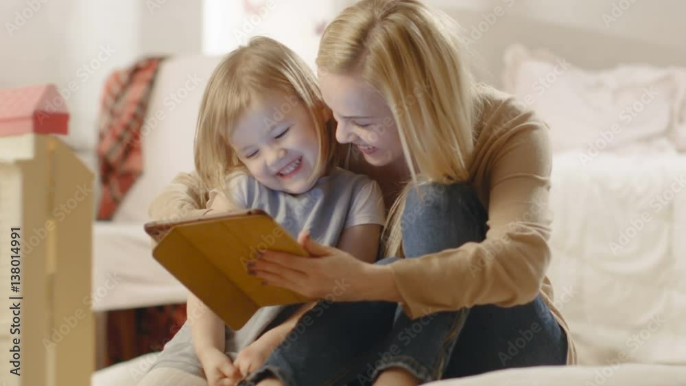 Beautiful Mother and Her Little Daughter Have Good Time Reading Children's Books on a Tablet Computer. Shot on RED EPIC-W 8K Helium Cinema Camera. Beautiful Mother and Her Little Daughter Have Good Time Reading Children's Books on a Tablet Computer. Shot on RED EPIC-W 8K Helium Cinema Camera.