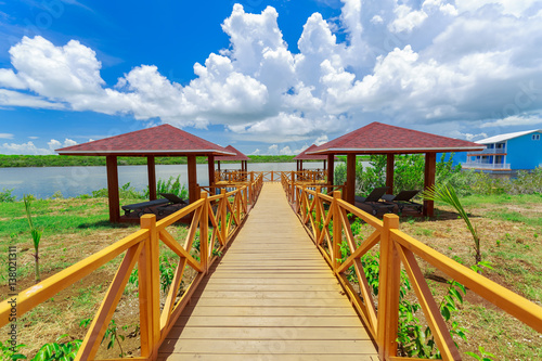 Stunning beautiful gorgeous view of wooden bridge toward beach gazebos in tropical garden park on sunny nice day photo