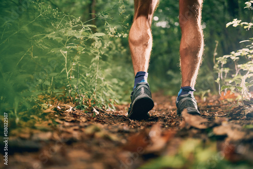 Muscular calves of a fit male jogger training for cross country forest trail race in nature park.