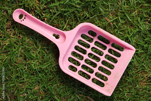 Used and dirty pink color cat litter scooper put on the grass floor represent the pet equipment material concept related idea.