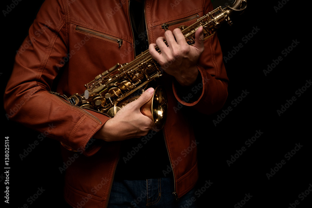 Obraz premium musician saxophone player holding his saxophone on isolated black background.