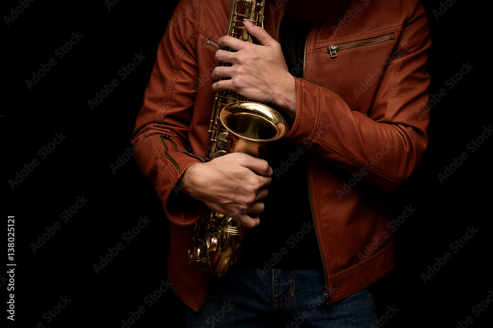Obraz premium musician saxophone player holding his saxophone on isolated black background.