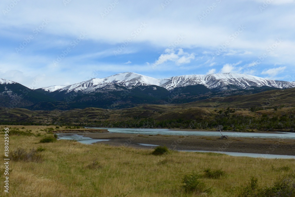 Fresh snow melt stream flowing through a beautiful open meadow surrounded by snow capped mountains in Torres del Paine National Park. 