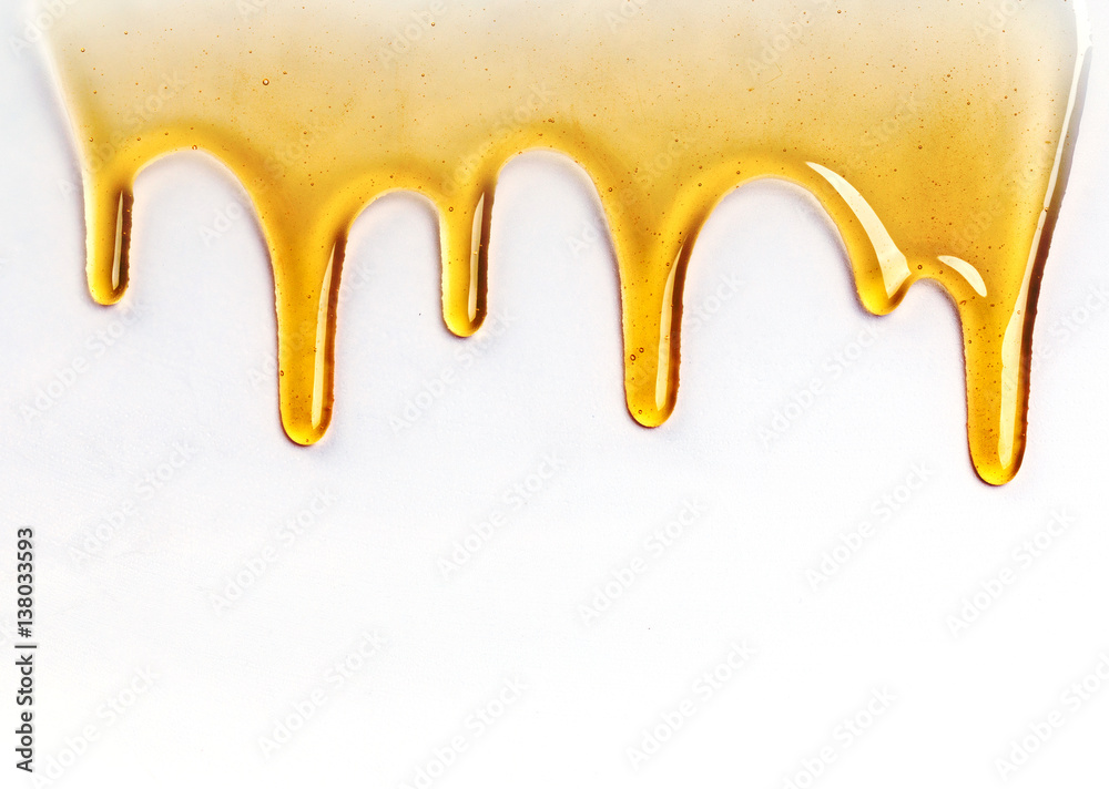 Dripping golden sweet honey flowing down the frame from the top over white with copyspace and text