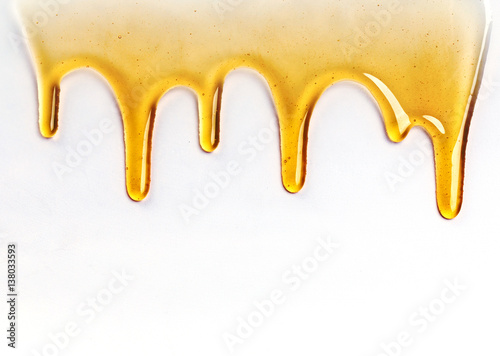 Fototapeta Naklejka Na Ścianę i Meble -  Dripping golden sweet honey flowing down the frame from the top over white with copyspace and text