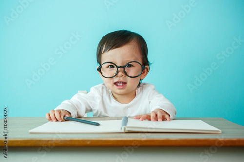 Asian baby girl smiling wearing glasses, on the table (soft focus on the eyes)