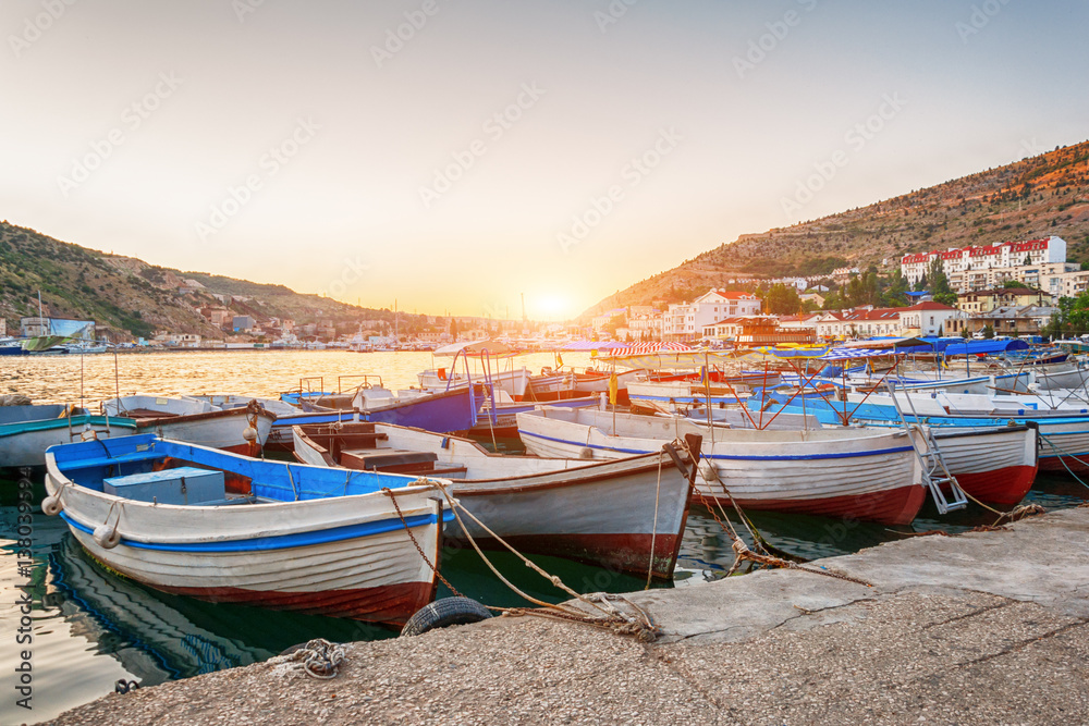 Sailing boats and yachts anchored in calm bay at sunset