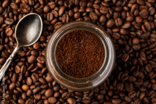 Metal spoon with coffee beans and ground coffee in a glass jar