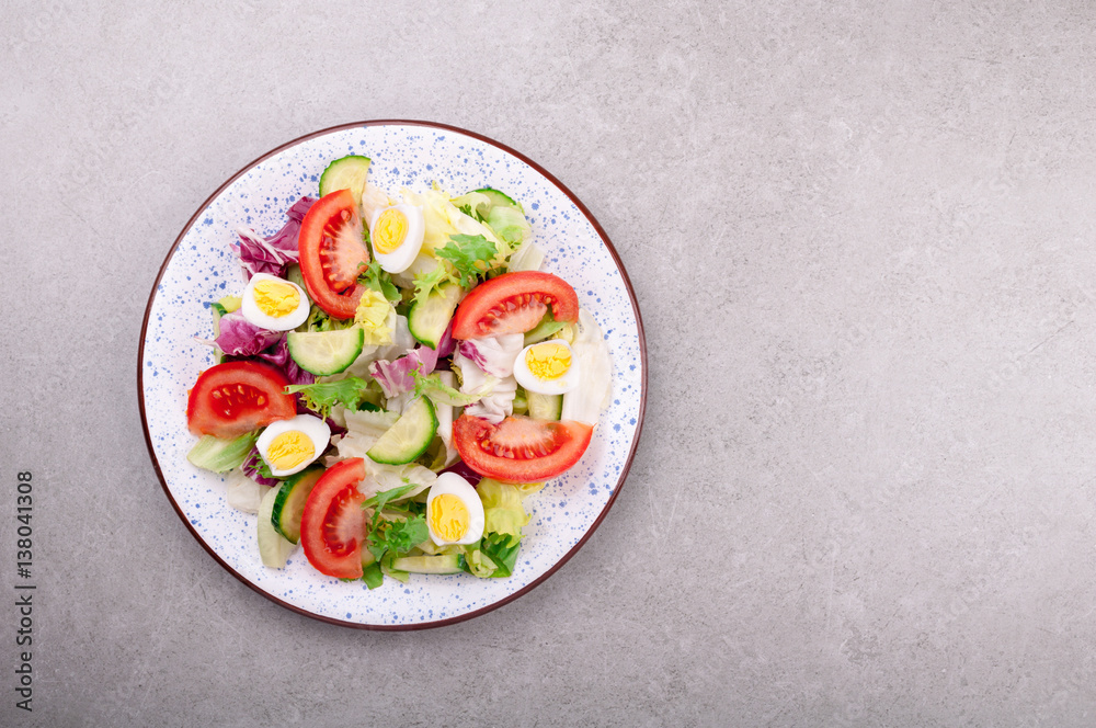 Fresh salad with vegetables tomatoes, cucumbers, lettuce, salad leaves and eggs on grey background top view and copy space. Healthy food and diet concept. Vegetarian food