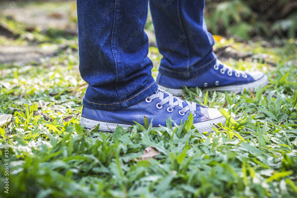 Man in blue sneakers and jeans standing on the green grass in the park.