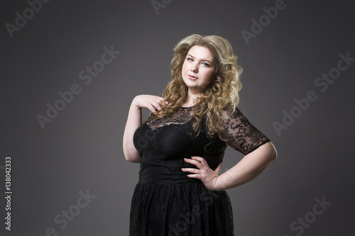 Young beautiful blonde plus size model in black dres, xxl woman portrait on gray studio background