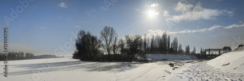 Panoramic photo of the frozen Tisa river covered with snow. Distant riverbanks veiled in mist.