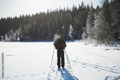 Skier tourist with a backpack on a frozen lake in the woods around the sun