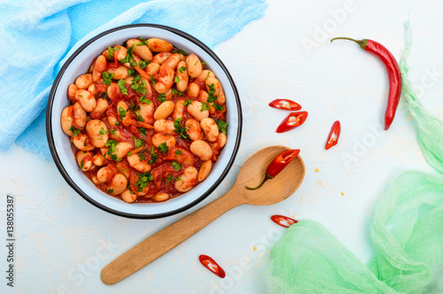 White large beans in sweet and sour tomato sauce in a bowl on a light background. The top view. Vegetarian cuisine. Lenten meal.