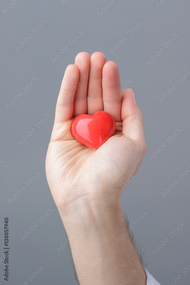 Fototapeta premium man in white shirt holds in hands red heart on gray background. 