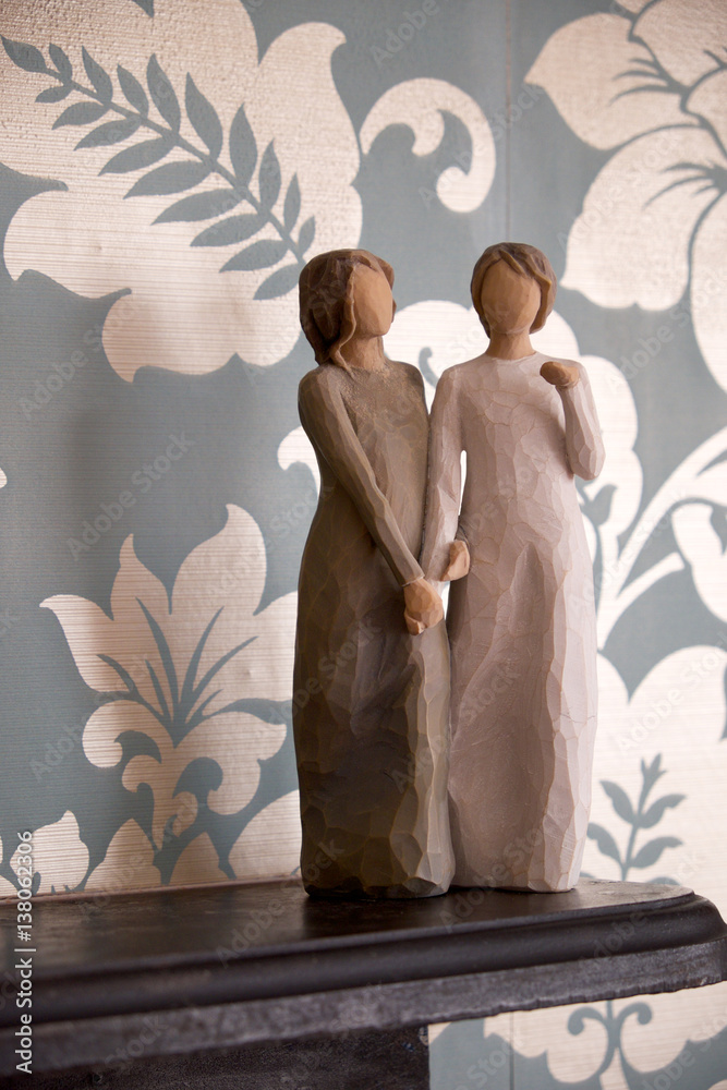 wooden statue of two women holding hands, statue is on a black ...