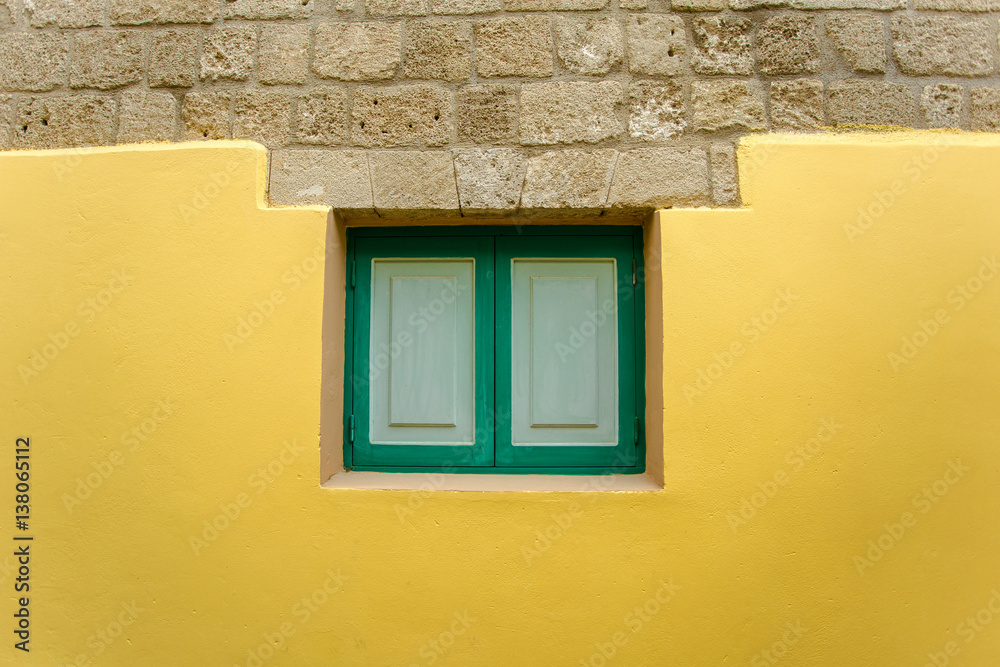 Green window on the yellow wall background, Rhodes, Greece.