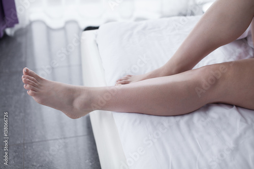 Bare legs of a young woman sleeping in her bed at home. Focus on legs.