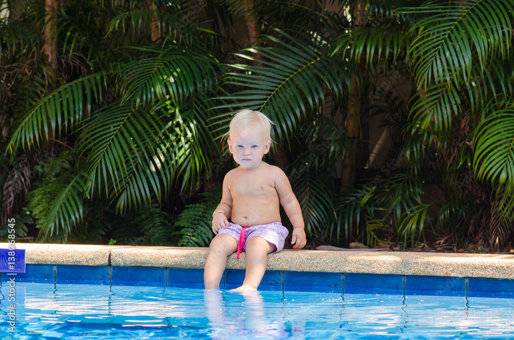 The child sits on the edge of the pool. Little baby is resting near the pool.