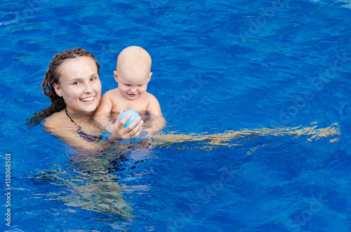Mother and her child in the pool. Woman playing with a ball with his little daughter.