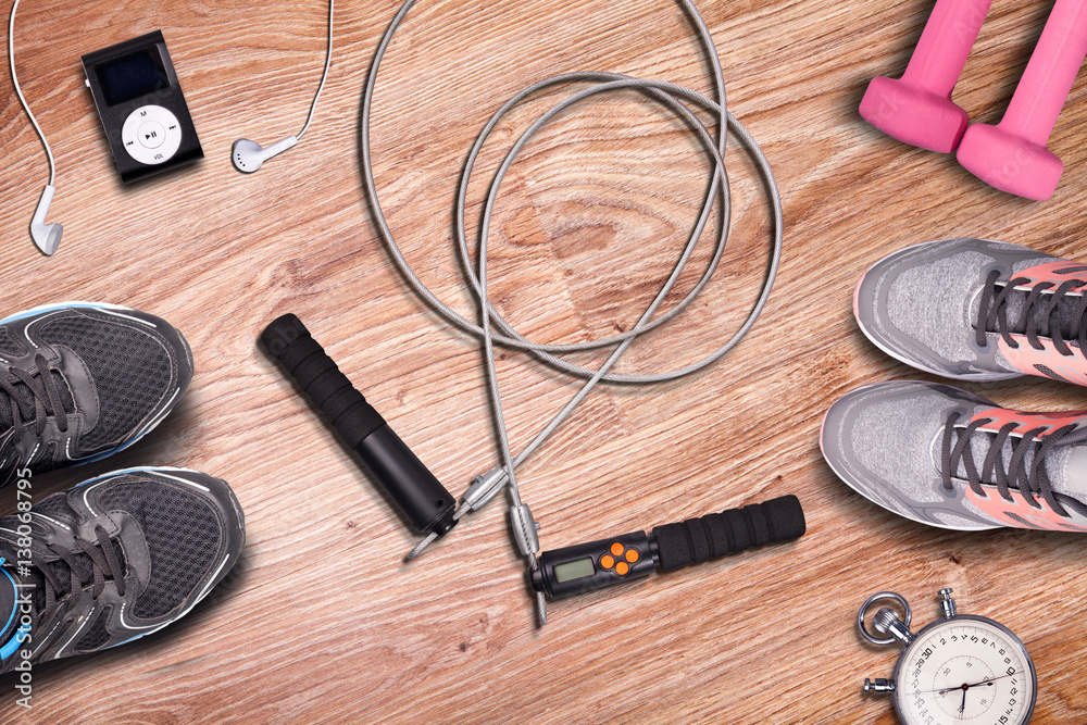 Gym mat and fitness accessories. Sport run shoes and jump rope. Light pink dumbbells on wood floor background.