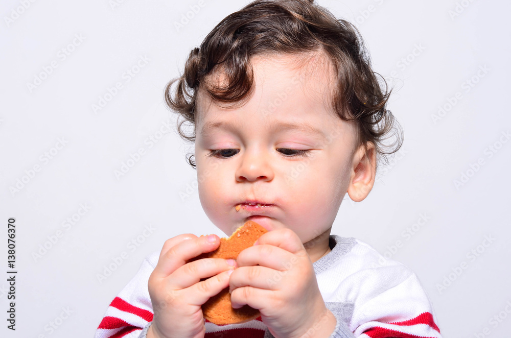 Portrait of a cute baby eating a biscuit. One year old kid eating biscuits by himself. Adorable curly hair boy being hungry. Portrait of a cute baby eating a biscuit. One year old kid eating biscuits by himself. Adorable curly hair boy being hungry.