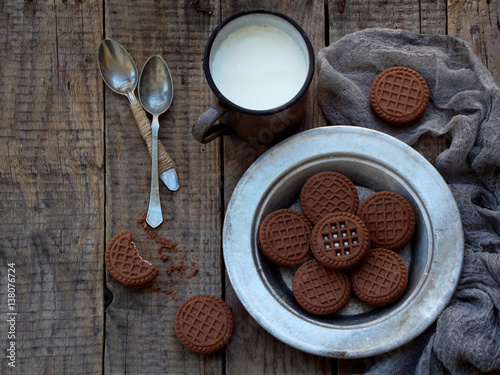 chocolate cookies with white cream and cup of milk on wooden background. Selective focus.