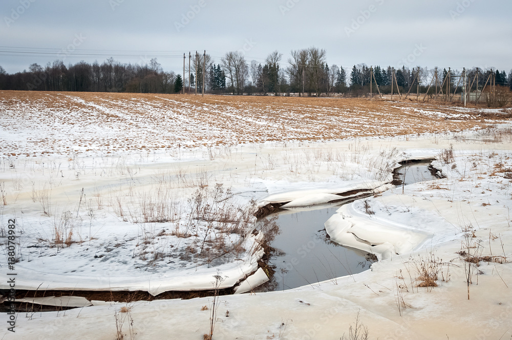 River between ice and snow covered fields. Yellowish fields with snow. River between ice and snow covered fields. Yellowish fields with snow.