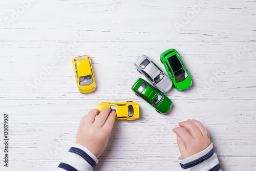 Foto Child hands playing with miniature toy cars, wooden background, top view