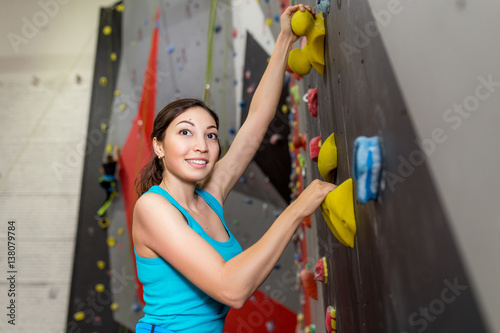 Fit sporty woman looking up at rock climbing wall at the gym and training