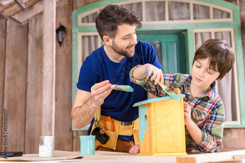 Canvas-taulu Happy father and son painting small wooden birdhouse on porch