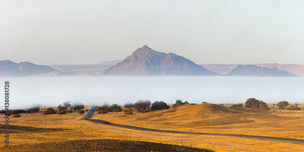 Obraz premium Fog over the tarred road crossing the Namib desert in Sossusvlei, Namib Naukluft National Park, in the misty morning.