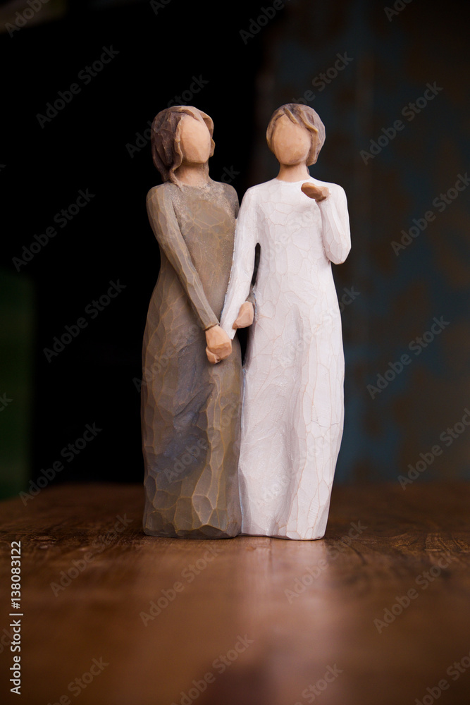 wooden statue of two women holding hands, statue is on a black ...