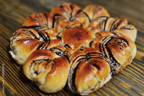 Fresh appetizing bun with poppy seeds on a wooden background close up