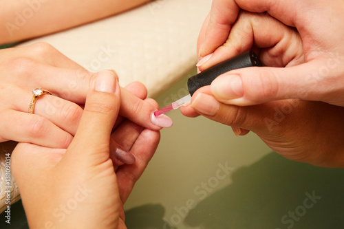 Closeup shot of a woman in a nail salon receiving a manicure by a beautician with nail file. Woman getting nail manicure. Beautician file nails to a customer photo