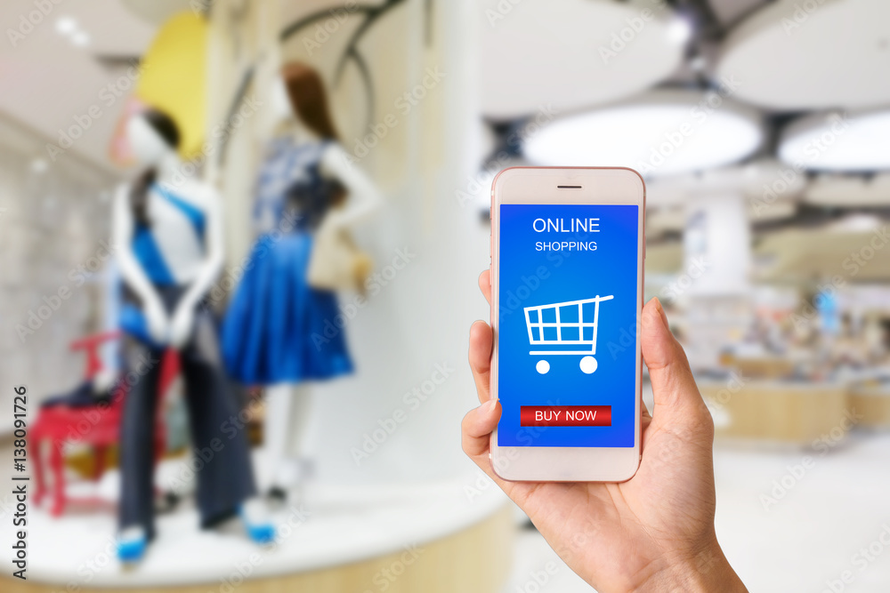 Woman hand holding smartphone against blur bokeh of shop background with word online shopping buy now