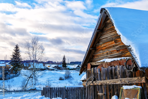 Snowy hills in Russian countryside in morning, red wooden house windows turned to east photo