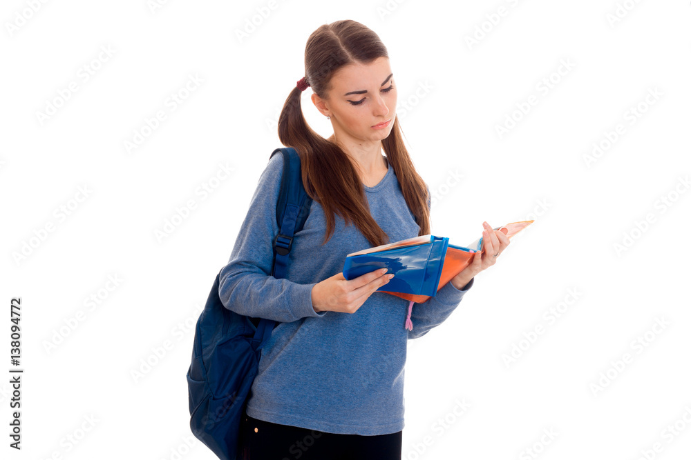 young smart brunette student girl with backpack on her shoulders reads a book isolated on white background young smart brunette student girl with backpack on her shoulders reads a book isolated on white background